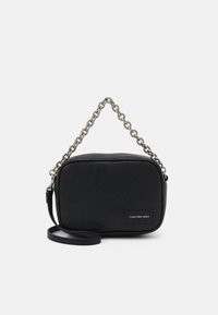 Borsa nera in tessuto con tracolla in catena argentata e tracolla nera regolabile. Presenta una toppa con logo sul fronte. Forma rettangolare.