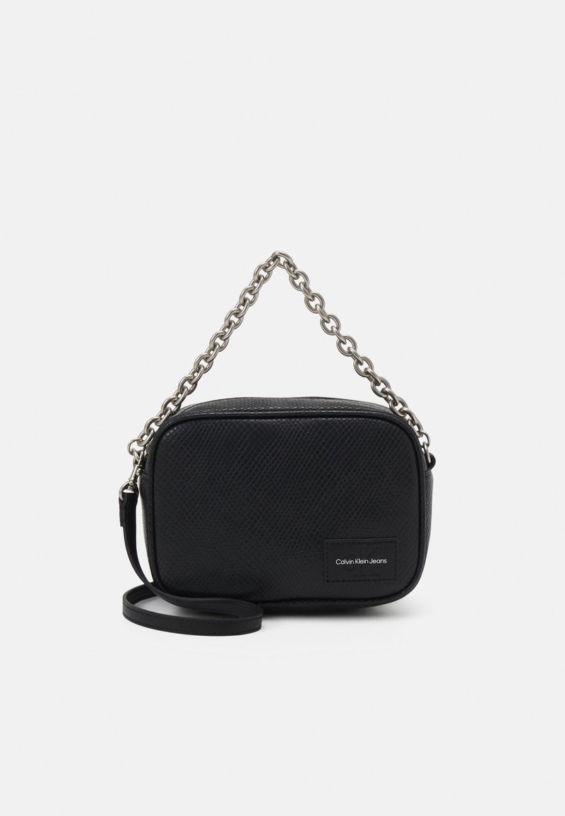 Borsa nera in tessuto con tracolla in catena argentata e tracolla nera regolabile. Presenta una toppa con logo sul fronte. Forma rettangolare.