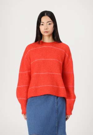 Un pull en maille rouge flou avec des rayures blanches, col rond et manches larges, associé à une jupe en jean bleu. Design texturé et décontracté.