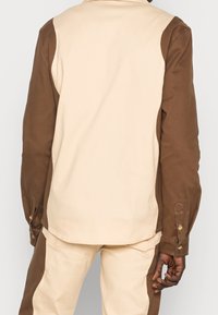 Brun och krämfärgad färgblockerad skjorta med avslappnad passform, som har kontrasterande ärmar, knäppta manschetter och en enkel kragsdesign.