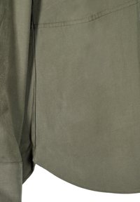 Olive green shirt detail featuring smooth fabric, curved hem, and side slits. The texture appears soft with subtle sheen.