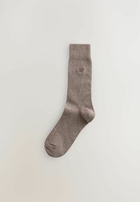 Braune gestrickte Socke mit einem gerippten Bund, glatter Textur und einem kleinen Logo nahe dem Knöchel. Sie hat ein klassisches, schlichtes Design.