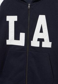 Marineblauwe hoodie met rits, grote witte gestikte letters "L" en "A" op de borst en pandzakken aan de voorkant.