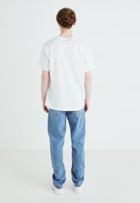 T-shirt bianco a maniche corte con scollatura rotonda, abbinato a jeans in denim azzurri e sneaker bianche e chunky, visto da dietro.