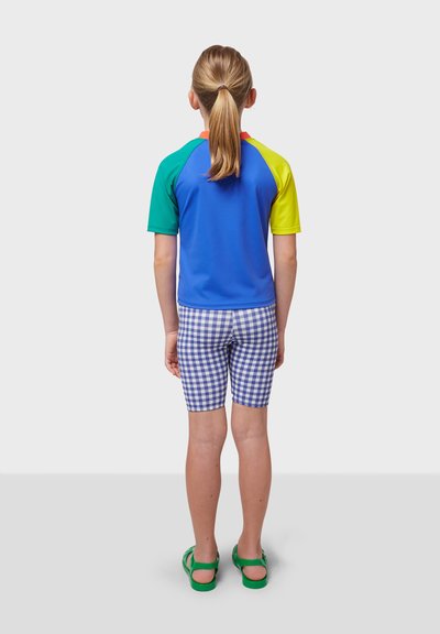 Färgglad rash guard med korta ärmar i blått, grönt, gult och rött, kombinerad med blå och vit rutiga badshorts och gröna sandaler.