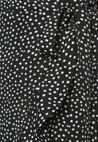 Tecido preto com bolinhas brancas, apresentando um detalhe de laço amarrado e acentos de babados, criando uma textura suave e em camadas.