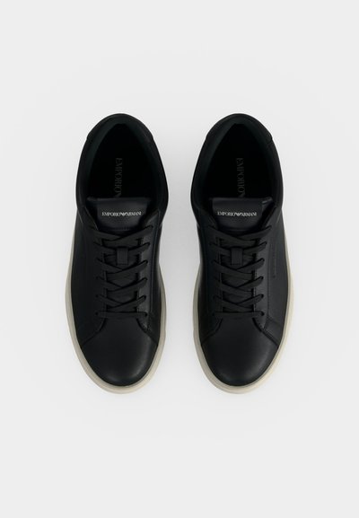 Paire de baskets basses noires Emporio Armani avec semelles blanches et lacets noirs vues de dessus sur fond blanc.