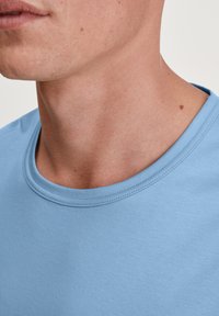 Lichtblauwe katoenen t-shirt met een ronde halslijn en een soepele textuur, met zichtbare stiksels langs de kraag en de zoom.