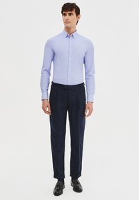 Jasnoniebieska koszula z długim rękawem z kołnierzykiem zapinanym na guziki, połączona z ciemnogranatowymi spodniami z zakładkami i czarnymi skórzanymi butami. Prosty design.