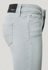 Vaqueros de mezclilla gris claro con un diseño ajustado, que presentan una etiqueta de marca negra en la cintura, pequeños bolsillos y costuras planas.