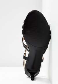 Sandalia negra de tacón con punta abierta, que cuenta con correas delgadas y una suela de textura suave. Marcado de tamaño visible en el tacón.