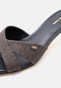 Sandale noire à talon avec larges brides croisées marron texturées et un petit détail logo métallique doré sur la sangle.