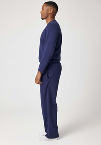 Completo da casa blu navy realizzato in tessuto morbido; maglia a maniche lunghe e pantaloni abbinati con fascia elastica in vita, mostrati di profilo.