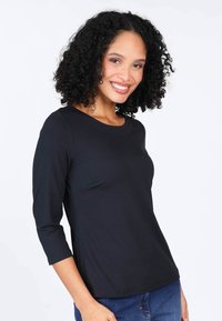 Black long-sleeve top made of soft fabric with a round neckline and fitted shape, paired with denim jeans. Smooth texture, casual design.