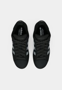 Ζευγάρι μαύρα αθλητικά παπούτσια Adidas με γκρι ρίγες και κορδόνια με σχέδια, σε άποψη από πάνω σε απλό λευκό φόντο.