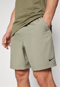 Nike athletic shorts in olive green, lightweight fabric, elastic waistband, side pockets, and small black logo detail on the hem.