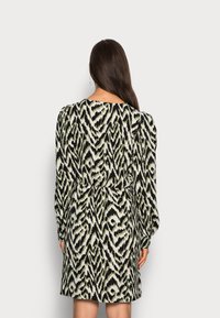 Vestido de mangas compridas com um padrão em zigzag preto, verde e branco; cintura ajustada; e costas plissadas para adicionar textura. Acabamento de tecido suave.