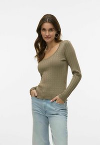 Olivgrön, rippad långärmad topp med rundad halsringning och scallop-kant. Matchad med ljusblå, avslappnade jeans.