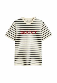 Camiseta a rayas en color crema, con rayas horizontales en azul marino y el logo bordado "GANT" en rojo en el centro. Diseño de mangas cortas y cuello redondo.