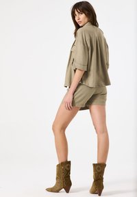 Khaki oversized shirt en bijpassende shorts gemaakt van lichte stof, gecombineerd met bruine geborduurde enkelboots met een spitse neus.
