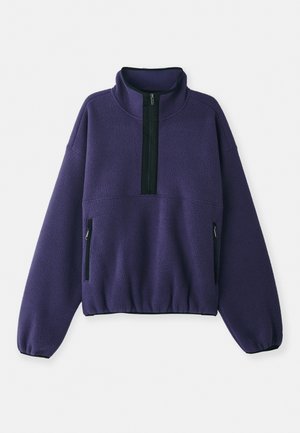 Pull en polaire violet avec un col à demi-fermeture éclair, fermeture éclair noire et poches latérales. Présente une coupe décontractée et des poignets élastiques. Texture douce.