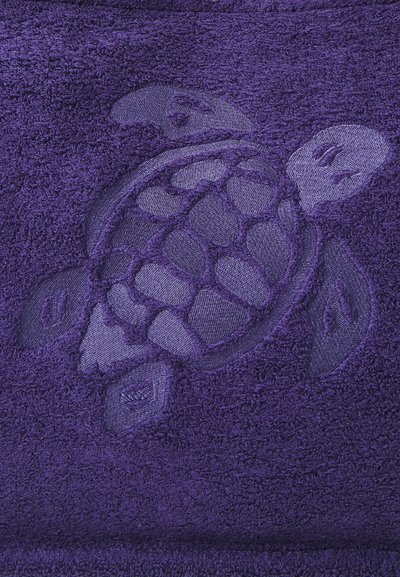 Lila Handtuch mit einem geprägten Schildkrötenmotiv in einem etwas helleren Farbton. Die Textur ist plüschig mit Schlaufenfasern, die Weichheit bieten.
