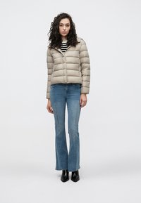 Svetlosivá bunda s prešívaním do vodorovných pruhov, so zapínaním na zips a kapucňou. Kombinovaná s modrými rozšírenými džínsami a čiernymi členkovými topánkami.