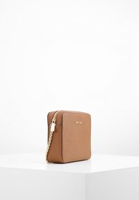Borsa in faux leather marrone con tracolla a catena dorata, forma rettangolare, chiusura con zip e logo embossato sul davanti.