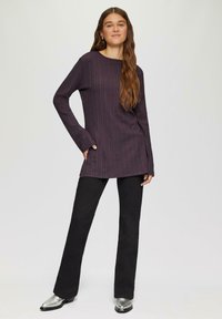 Langärmliges, dunkelviolettes, geripptes Oberteil mit Rundhalsausschnitt, kombiniert mit schwarzen Schlaghosen und glänzenden silbernen Stiefeletten.