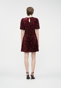 Φόρεμα μπορντό με παγιέτες και μανίκια puff, που διαθέτει κωδικό πίσω. Φοριέται με μαύρες ψη�λές γόβες με λουράκια. Λείος υφασμάτινος χαρακτήρας, εφαρμοστή σιλουέτα.