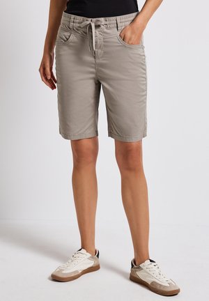 Lichtgrijze shorts met een elastische tailleband, trekkoord, zijzakken en een ontspannen pasvorm. Gepaarde met witte en beige sneakers.
