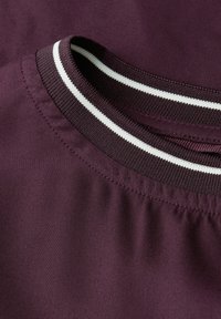 Tejido de jersey burdeos con un cuello acanalado que presenta franjas blancas y negras. Textura suave con un diseño de corte relajado.