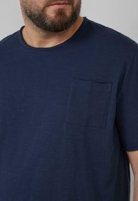 Marineblauwe T-shirt met korte mouwen, gemaakt van zachte stof, met een vierkante borstzak en zichtbare stikdetails.