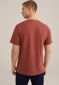 T-shirt krátký rukáv v rezavé barvě s texturovaným žebrovaným vzorem, kulatým výstřihem a rovnými lemy, v kombinaci s tmavými džínami.