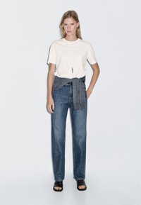 Vit kortärmad t-shirt i kombination med ljusblå hög midja jeans, en grå tyg knuten i midjan, och svarta sandaletter med öppen tå.