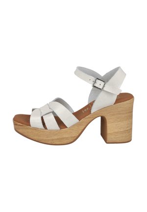 Sandalias de tacón de cuero blanco con un tacón de bloque de madera, que cuentan con correas cruzadas y una correa en el tobillo con una hebilla plateada.