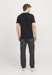 T-shirt noir à manches courtes, en coton, coupe décontractée, porté avec un jean en denim foncé, vu de dos, design simple, détails minimaux.