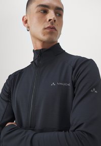 Mustast viimistletud jakist, mis on valmistatud kerge kangaga. Omab kõrget krae, diskreetset logo rinnal ja saledat, hästi istuvat disaini.