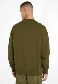 Sudadera verde oliva con un corte relajado, puños y dobladillo acanalados, y un detalle de costura en V en la parte posterior. Tejido suave con una textura lisa.