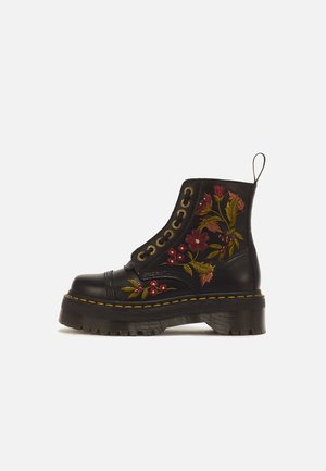 Botte en cuir noir à lacets avec semelle épaisse, avec une broderie florale rouge et jaune sur le côté et une languette à l'arrière.