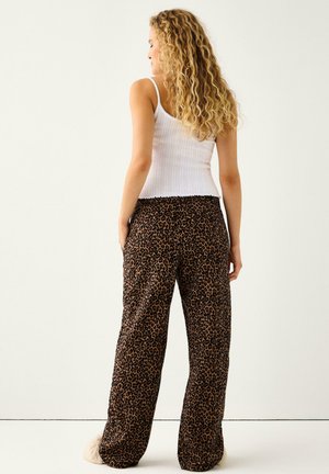 Laza szabású, könnyű anyagú, leopárdmintás nadrág gumis derékrésszel. Bordázott fehér trikó, melyet a deréknál be van tűrve.