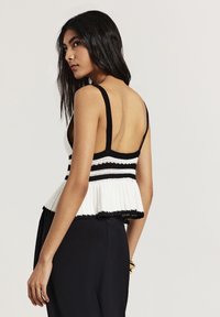 Top peplum a maglia con un design a righe bianche e nere, spalline larghe, schiena scoperta, tessuto testurizzato e orlo scallopato.