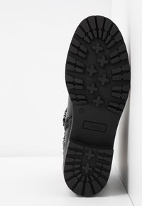 Suela de bota de combate negra con un patrón de textura, que presenta formas de cruz elevadas y el logo de la marca "ONLY" en relieve. Indicado tamaño 37.