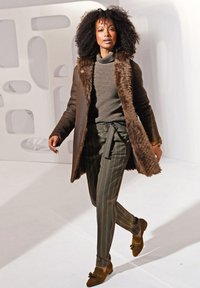 Bruin leren jas met een nep bontkraag, groene gestructureerde trui, gestreepte broek en bruine loafers met strikaccenten, met een strakke pasvorm.