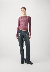 Lilla grafisk tanktopp i lag med en langermet burgunder topp, parret med mørke denimbukser med belte med sølvspenner og nagler.