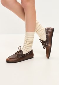 Mocasini din piele maro cu vârf rotunjit, sistem de șireturi frontal și urechi laterale, asortați cu șosete crem cu model cu nervuri. Design cu talpă plată.