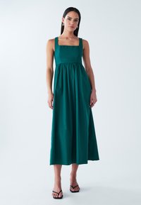 Smaragdiroheline maksikleit ruudukujulise kaelusega, kogutud vöökohaga ja voolava seelikuga. Valmistatud kergest kangast, millel on laiad õlapaelad.