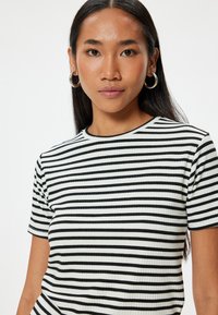 Camiseta de rayas en blanco y negro, de canalé, con mangas cortas y escote redondo, con una textura en la tela. El modelo muestra la vista frontal.