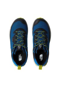 Μπλε αθλητικά παπούτσια με υφή στην επάνω επιφάνεια, μαύρες λεπτομέρειες, φωτεινά κίτρινα κορδόνια και αντίθετο ταμπελάκι στη φτέρνα. Σχεδιασμένα για χρήση σε εξωτερικούς χώρους.