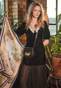 Črna žametna obleka z nabranimi rokavi in čipkastim izrezom, v kombinaciji s vzorčasto svilenim šalom in majhno črno torbico z rožnim vezenjem.